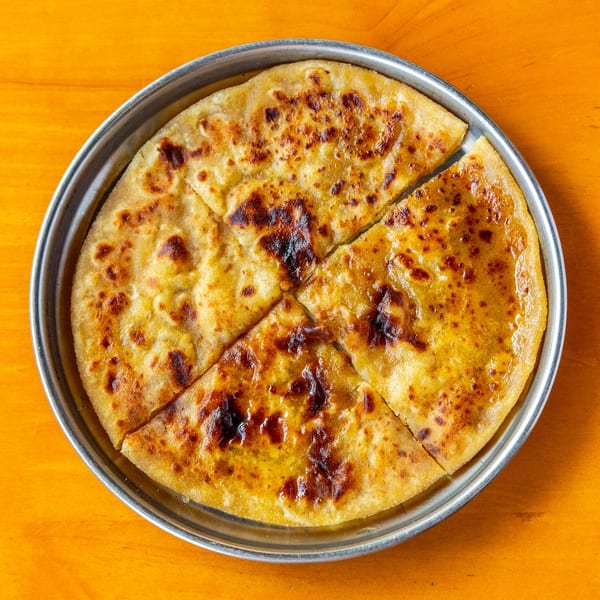 Golden-brown paratha, cut into four triangular pieces, served on a silver plate.