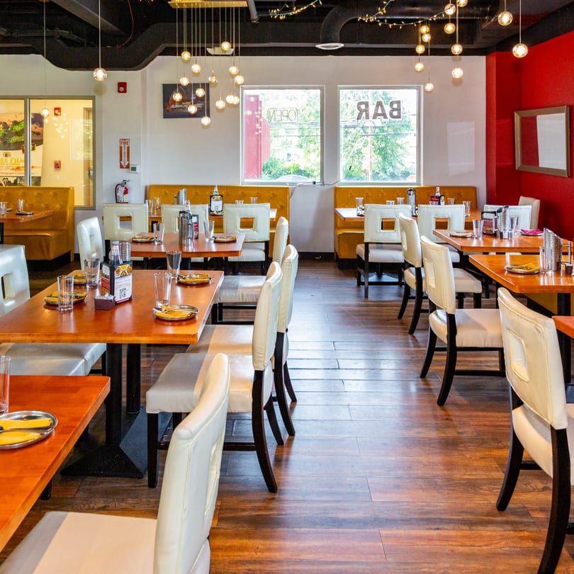 Restaurant interior with wooden tables, white chairs, yellow booths, and red accent walls.