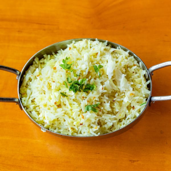 A metal bowl filled with white rice, garnished with green herbs, on a wooden table.