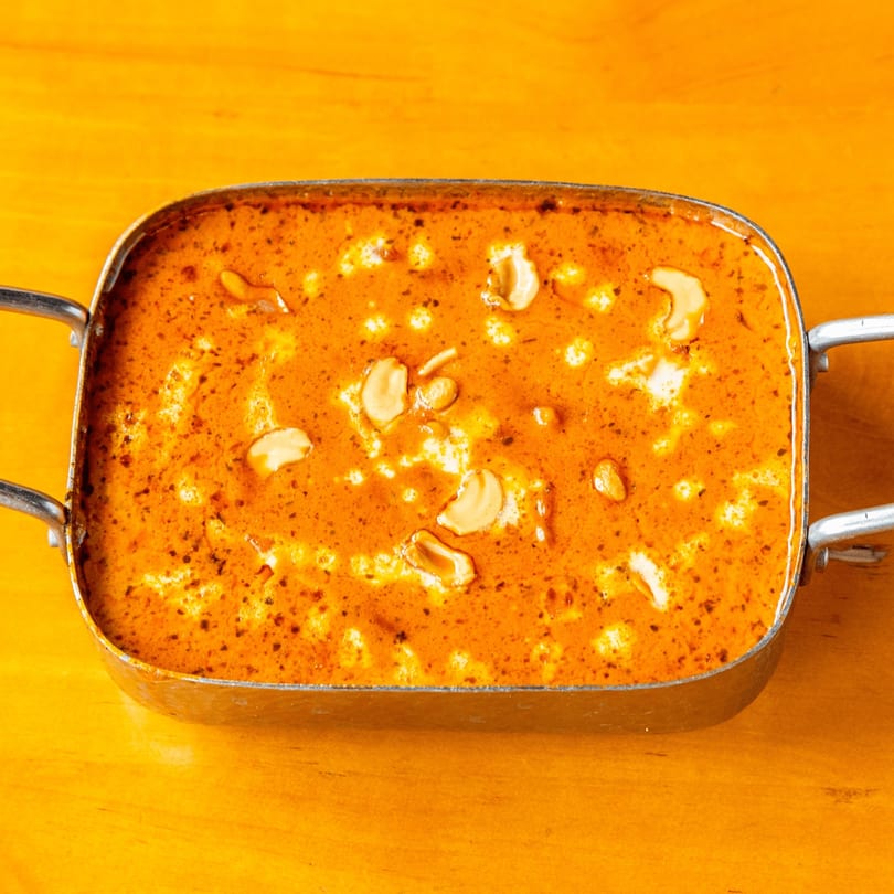 A metal serving dish filled with a rich orange curry, garnished with cashews and cream.