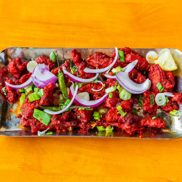 Spicy red chicken 65 appetizer with onions, green chilies, and lemon on a metal tray.