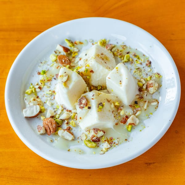 White dessert squares drizzled with syrup and topped with chopped pistachios and almonds on a white plate.
