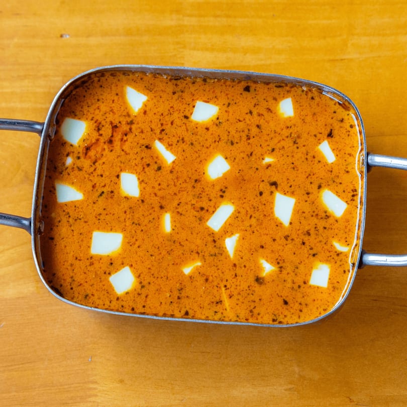 Overhead view of paneer butter masala, a creamy orange curry with white paneer cubes, in a metal serving dish.