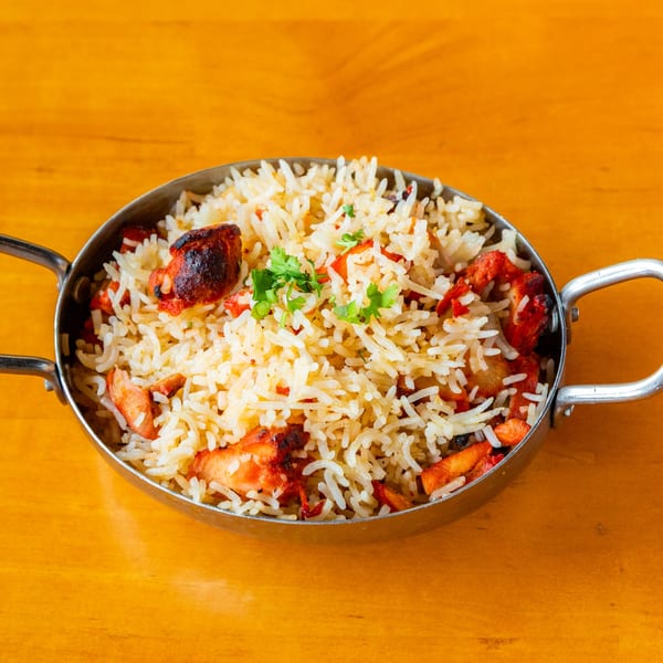Chicken biryani with cilantro in a metal serving dish on a wooden table.