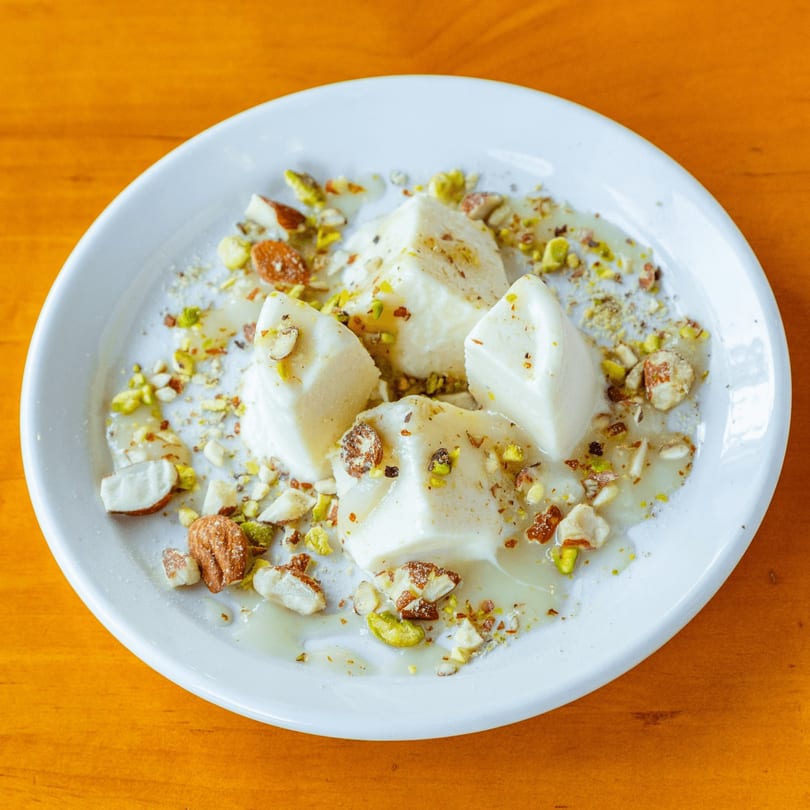 White dessert squares drizzled with syrup and topped with chopped pistachios and almonds on a white plate.