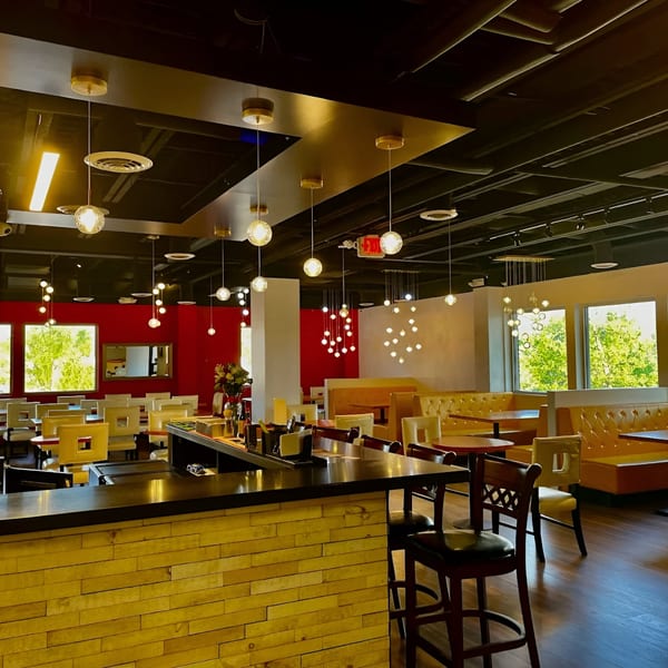 Modern Indian restaurant interior with red walls, yellow booths, a bar, and hanging spherical lights.