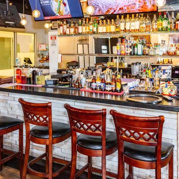 A well-stocked bar with various liquor bottles, beer, and bar stools, featuring a brick-patterned counter.