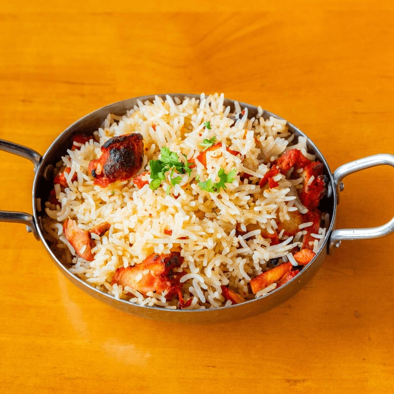 Chicken biryani in a metal serving dish, garnished with fresh cilantro on a wooden table.