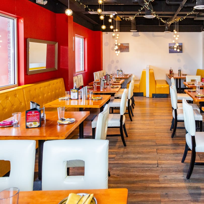 Restaurant interior with red walls, yellow booths, wooden tables, white chairs, and string lights.
