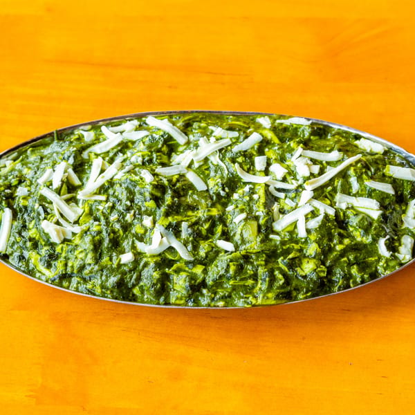 Creamy green spinach dish, possibly saag paneer, topped with white cheese crumbles in a silver dish.