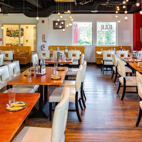 A restaurant dining room with wooden tables, white chairs, yellow booths, and hanging globe lights.